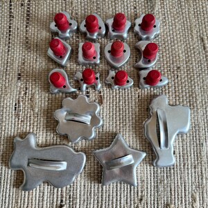 May include: A collection of metal cookie cutters in various shapes, including stars, hearts, animals, and flowers. The smaller cutters feature red wooden handles, while the larger cutters have simple metal loops for gripping and handling.