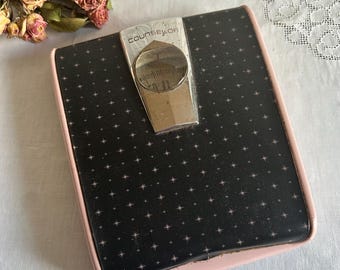 May include: Vintage black and pink bathroom scale with a starburst pattern. The scale has a silver-colored dial and the word "COUNSELOR" is printed on the top. The scale has a pink border.