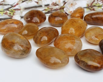 May include: A collection of tumbled citrine stones in various shades of yellow and brown. The stones are smooth and polished, with a natural, organic shape.