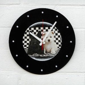 May include: Black and white round wall clock featuring a black and white checkered background with two dogs. The clock has a black frame with silver studs and white clock hands. The second hand is red.