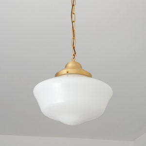 May include: A gold pendant light with a white glass shade. The light is hanging from a chain.