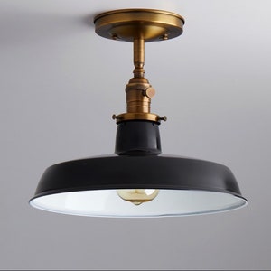 May include: A black metal ceiling light fixture with a white interior and a brass finish. The light has a simple, industrial design.