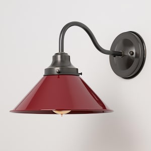 May include: A wall-mounted light fixture with a deep red, conical shade and a dark gray, curved arm. The fixture has a circular base and a vintage industrial design.