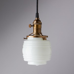 May include: A white glass pendant light with a brass finish and a black cord. The glass shade has a ribbed design.