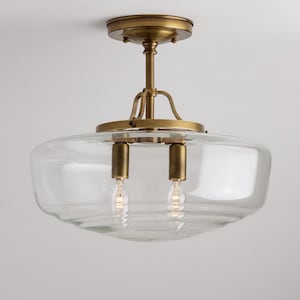 May include: A brass ceiling light fixture with a clear glass shade. The shade has a rounded, bowl-like shape and features two light bulbs.
