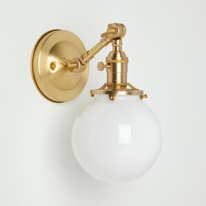 May include: A brass wall sconce with a white globe shade. The sconce has a swivel arm and a vintage-style socket.