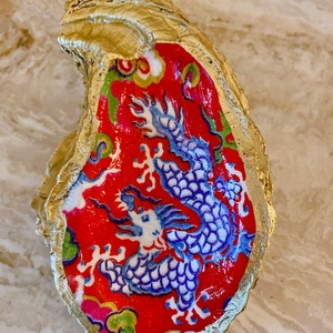 May include: A gold oyster shell with a red and blue dragon design. The dragon is painted in a traditional Chinese style with intricate details.