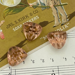Pode incluir: Quatro contas de vidro facetadas, em tons de rosa, estão espalhadas em um cartão vintage com uma ilustração floral e partituras. O cartão diz "JAS. S. KIRK & CO. SOAP MAKERS".