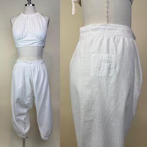 May include: White two-piece outfit featuring a halter top and harem pants. The top has a gathered bust and ties at the neck. The pants are loose-fitting with a gathered ankle and a single pocket on the back. The outfit is displayed on a mannequin.