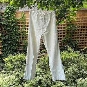 May include: Off-white trousers featuring a straight-leg cut, a high-rise waist with an elasticated waistband, and a functional drawstring tie at the centre front. The trousers are constructed with visible vertical seams and a clean, simple hemline.