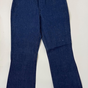 Pode incluir: Cal&ccedil;as de ganga azul escuro com design de perna larga. As cal&ccedil;as de ganga t&ecirc;m um estilo cl&aacute;ssico de cinco bolsos com costuras cor de cobre e fecho de bot&atilde;o. O tecido parece ser ganga de peso m&eacute;dio.