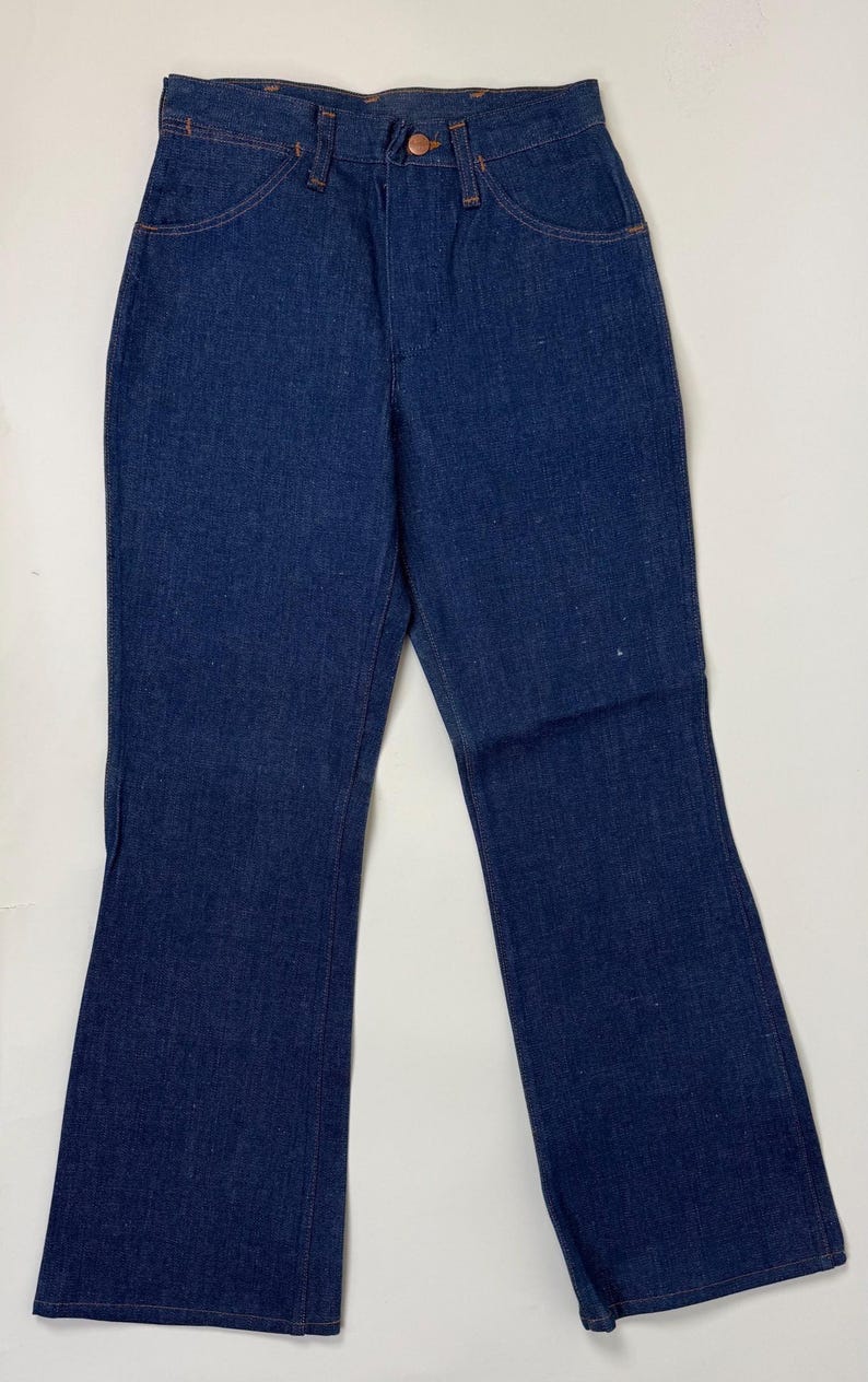 Pode incluir: Cal&ccedil;as de ganga azul escuro com design de perna larga. As cal&ccedil;as de ganga t&ecirc;m um estilo cl&aacute;ssico de cinco bolsos com costuras cor de cobre e fecho de bot&atilde;o. O tecido parece ser ganga de peso m&eacute;dio.