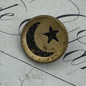 May include: A gold-colored button with a black crescent moon and star design.