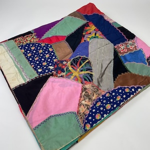 May include: A patchwork quilt made of various fabrics in shades of blue, green, pink, red, brown, and white. The quilt is made of squares and rectangles of fabric sewn together with a zig-zag stitch.