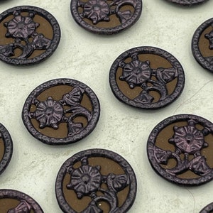 May include: A collection of 12 round, brown, metal buttons with a floral design. The buttons have a raised, ornate design with a purple hue.