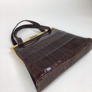 May include: A brown leather handbag with a gold frame and a top handle. The bag has a crocodile-embossed pattern.