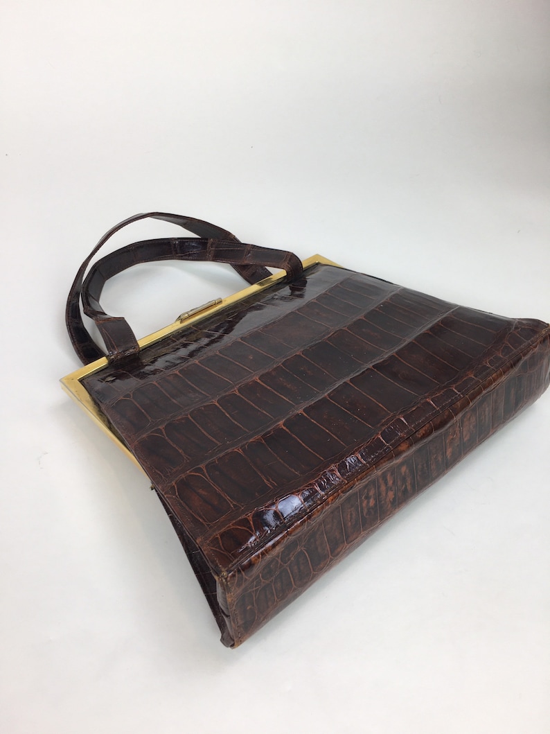 May include: A brown leather handbag with a gold frame and a top handle. The bag has a crocodile-embossed pattern.