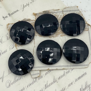 May include: Six black buttons with a geometric pattern. The buttons are round and have a shiny finish.