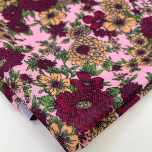 May include: Pink fabric with a floral print featuring red, yellow, and green flowers. The fabric has a textured surface.