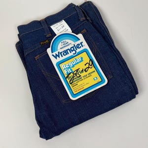 Puede incluir: Vaqueros Wrangler azul oscuro doblados con etiqueta. La etiqueta dice "Regular Fit" y "28 x 29". La etiqueta tambi&eacute;n indica "100% Algod&oacute;n 14 Onzas Denim". Los vaqueros son pre-encogidos.