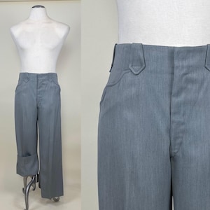 Pode incluir: Calças cinza claro com pernas largas e bainha dobrada. As calças são exibidas em um manequim. A cintura apresenta um design exclusivo com detalhes pontiagudos nos bolsos. O tecido parece ser um material liso e tecido.