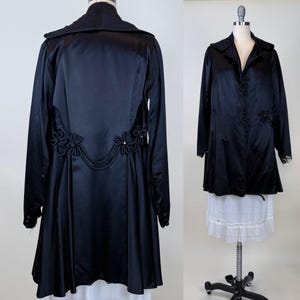 May include: A white ceramic mug with a black handle and the text "But First, Coffee" in a bold, black font. The mug is set against a blurred background. The mug appears to be approximately 10 cm tall.