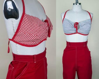 May include: A two-piece outfit featuring a halter top and high-waisted pants. The halter top is red and white gingham, trimmed with red. The pants are solid red with white stitching. The outfit is displayed on a mannequin.