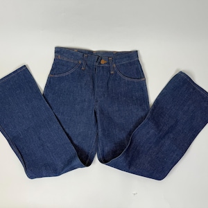 Pode incluir: Cal&ccedil;as de ganga azul escuro com cintura alta e pernas largas. As cal&ccedil;as de ganga t&ecirc;m um estilo cl&aacute;ssico de cinco bolsos, fecho de bot&atilde;o e z&iacute;per, e s&atilde;o feitas de um tecido de ganga resistente. As cal&ccedil;as de ganga s&atilde;o de estilo vintage.