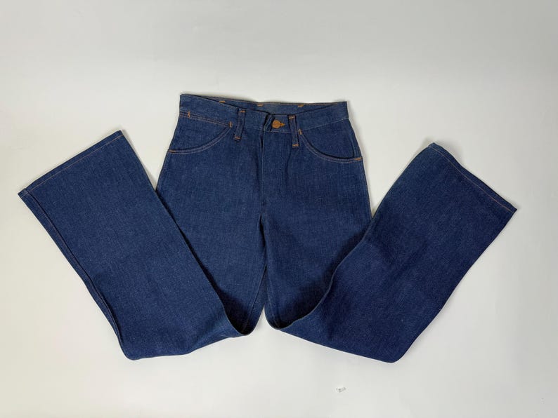 Pode incluir: Cal&ccedil;as de ganga azul escuro com cintura alta e pernas largas. As cal&ccedil;as de ganga t&ecirc;m um estilo cl&aacute;ssico de cinco bolsos, fecho de bot&atilde;o e z&iacute;per, e s&atilde;o feitas de um tecido de ganga resistente. As cal&ccedil;as de ganga s&atilde;o de estilo vintage.
