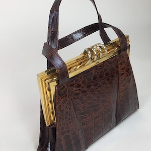 May include: A brown leather handbag with a gold clasp and a crocodile-embossed design.