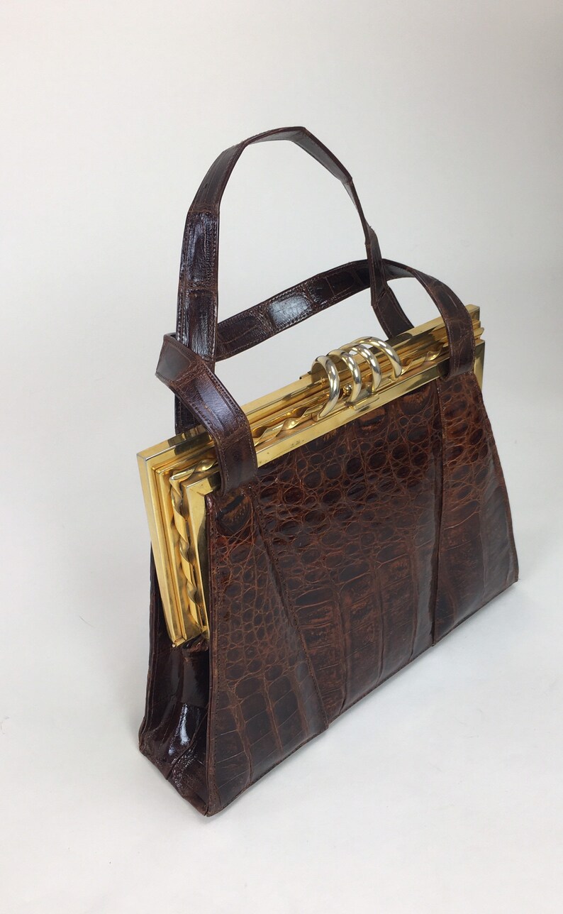 May include: A brown leather handbag with a gold clasp and a crocodile-embossed design.