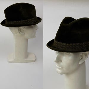 May include: A dark green fedora hat with a patterned band. The hat is displayed on a white mannequin head, showcasing its shape and design. The hat's brim is slightly curved, and the crown has a classic teardrop shape.