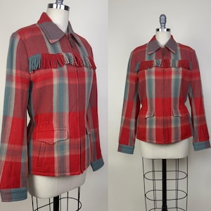 May include: A red, blue, and tan plaid jacket with a gray collar and fringe detail. The jacket has a zipper closure, two front pockets, and blue cuffs. The jacket is displayed on a mannequin.