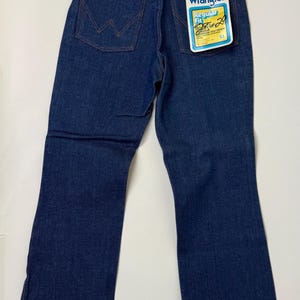 Puede incluir: Vaqueros Wrangler azul oscuro de corte Regular Fit con etiqueta. Los vaqueros tienen un dise&ntilde;o cl&aacute;sico de cinco bolsillos, cremallera y el logo de Wrangler en el bolsillo trasero. La etiqueta indica una cintura de 76 cm y un largo de 74 cm.