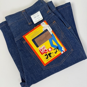Pode incluir: Cal&ccedil;as de ganga azul escuro com uma etiqueta "Wrangler". A etiqueta amarela apresenta "Flare Leg Jeans" e o tamanho "28x29" (aproximadamente 71x74 cm). As cal&ccedil;as de ganga est&atilde;o dobradas, mostrando os bolsos traseiros e a cintura. As cal&ccedil;as s&atilde;o pr&eacute;-encolhidas e 100% algod&atilde;o.