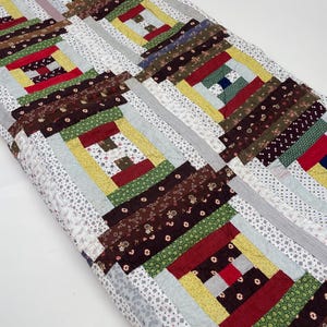 May include: A patchwork quilt with a log cabin pattern in shades of brown, green, red, and yellow. The quilt is made of various fabrics with different patterns, including floral prints and stripes.