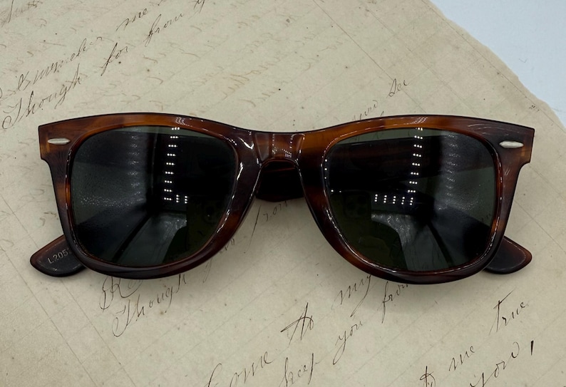 May include: Brown tortoiseshell sunglasses with dark lenses. The classic frames have a rectangular shape and are set against a vintage paper background. The sunglasses have a timeless design.