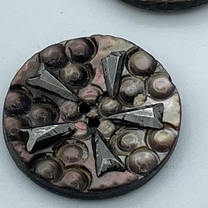 May include: A round, dark brown, iridescent button with a raised, textured design of circles and five silver-colored arrowheads.