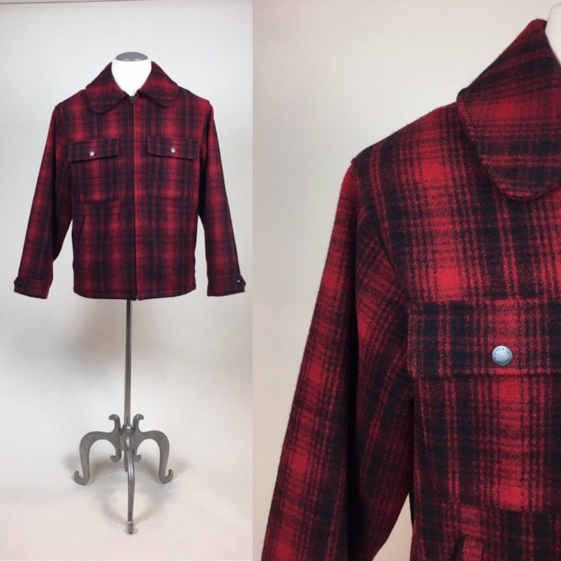 May include: A red and black plaid jacket with a full zipper closure, two chest pockets, and a collared neckline. The jacket is displayed on a mannequin. The fabric has a textured appearance.