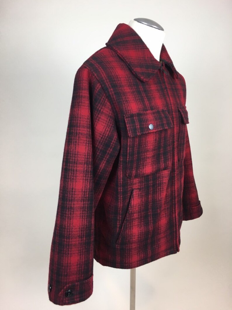 May include: A red and black plaid jacket with a collared neckline and two front pockets. The jacket has a zipper closure and buttoned cuffs. The fabric appears to be a thick, warm material, suitable for cooler weather.