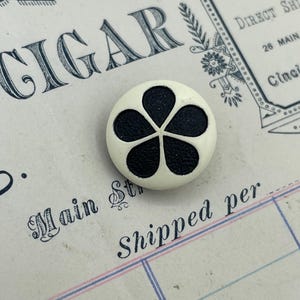 May include: White button with a black five-petal flower design.