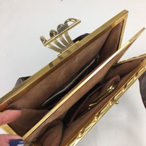 May include: A brown leather purse with a gold clasp and a gold chain strap. The purse is open and the inside is lined with brown fabric.