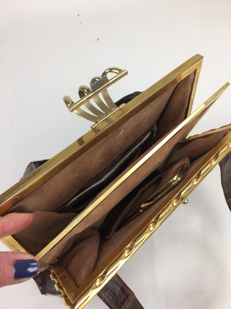 May include: A brown leather purse with a gold clasp and a gold chain strap. The purse is open and the inside is lined with brown fabric.