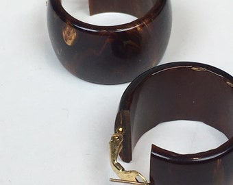 May include: A pair of dark brown hoop earrings with a marbled effect and gold-coloured clasps. The earrings have a thick, rounded design. Each earring is a chunky hoop.
