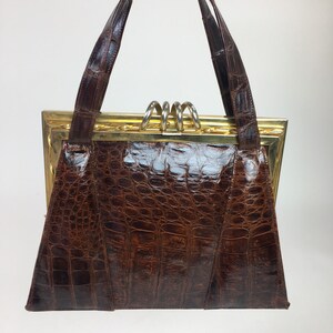 May include: A brown leather handbag with a gold frame and a top handle. The bag has a crocodile-embossed texture.