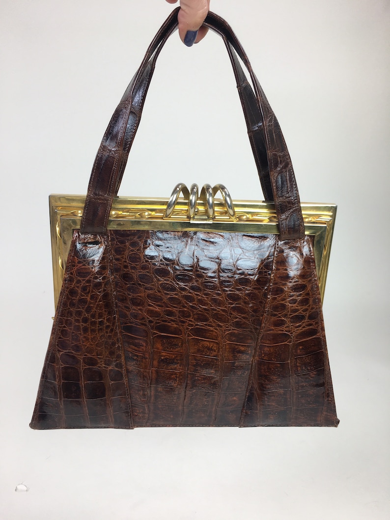 May include: A brown leather handbag with a gold frame and a top handle. The bag has a crocodile-embossed texture.