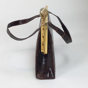 May include: A brown leather handbag with a gold clasp and a chain strap. The bag has a rectangular shape and is made of a textured leather.
