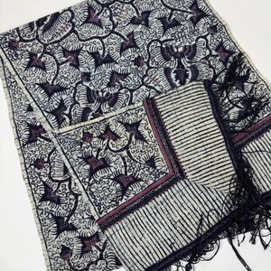May include: A patterned textile featuring a repeating design of stylized birds in shades of purple and black on a cream background. The textile includes a fringed edge and a striped border. The overall design has a vintage or ethnic aesthetic.