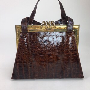 May include: A brown crocodile embossed leather handbag with a gold metal frame and a top handle.