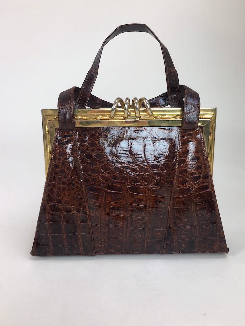 May include: A brown crocodile embossed leather handbag with a gold metal frame and a top handle.